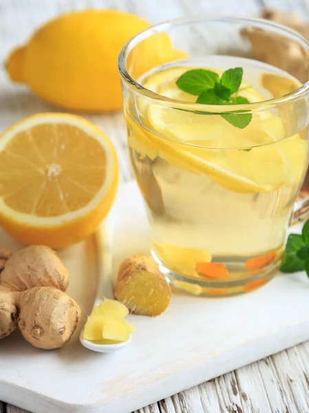 glass of ginger lemon zest tea displayed next to ginger root, lemons, and mint 