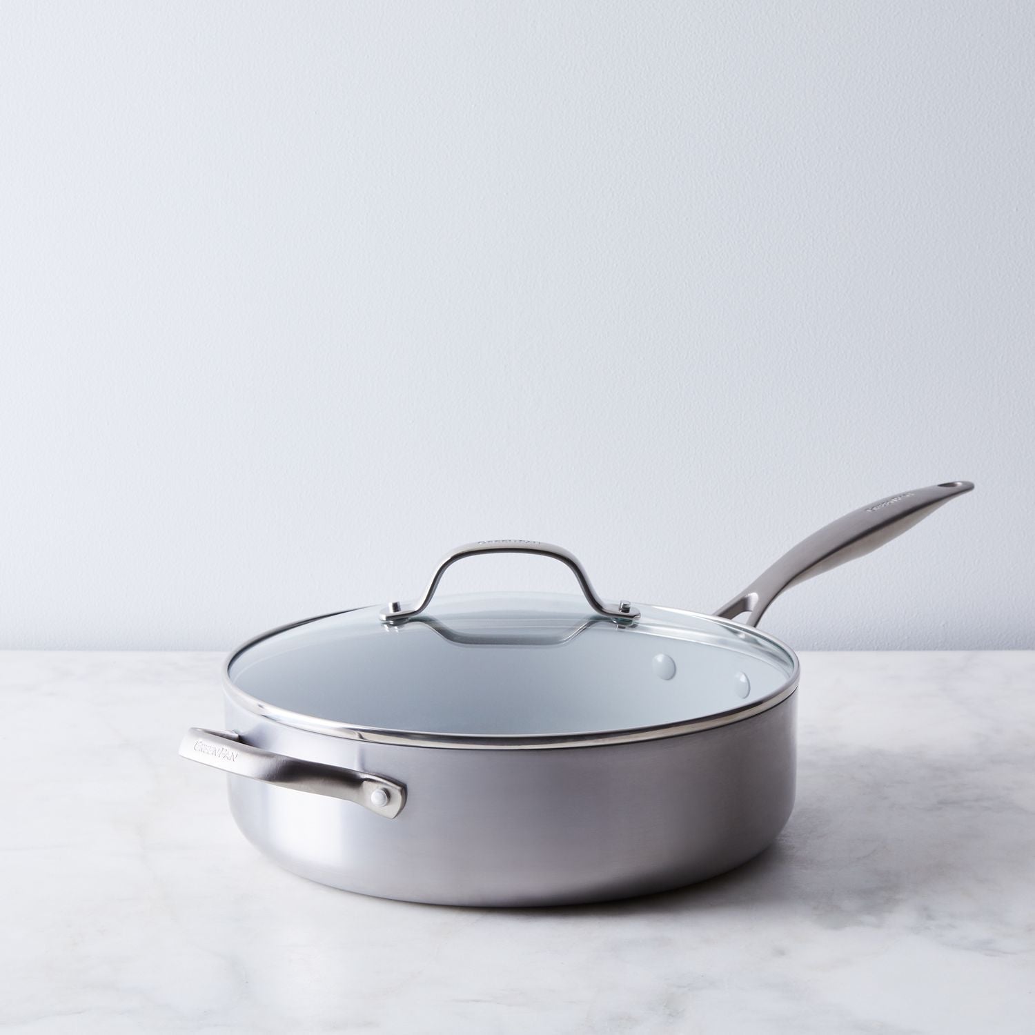 saute pan with lid on marble counter with white background.