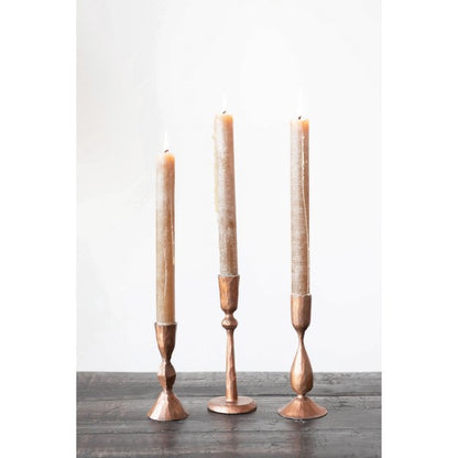 three iron taper holder with copper finish displayed on a dark stained table against a white background