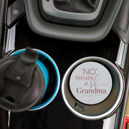 top view of the no means ask grandma car coaster displayed in the cup holder in a car