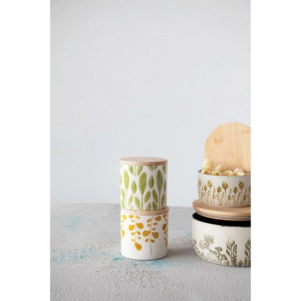 two hand stamped stoneware jars with lids displayed next to two stacked bowls with lids against a white background