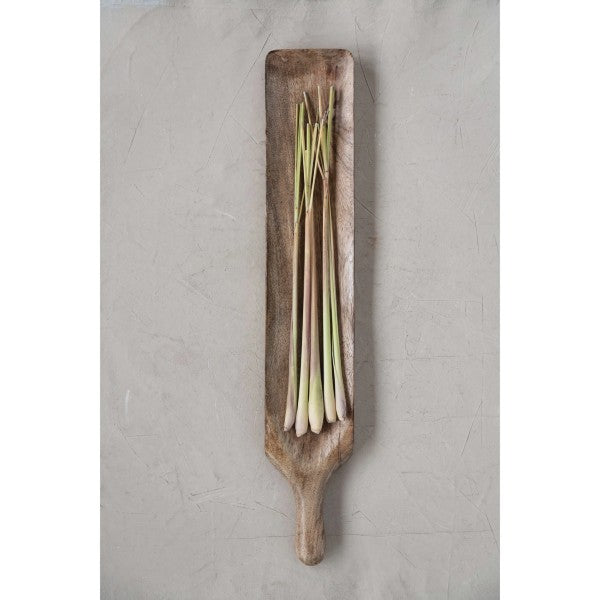 mango wood serving board with handle displayed on a light gray surface with green onions on it
