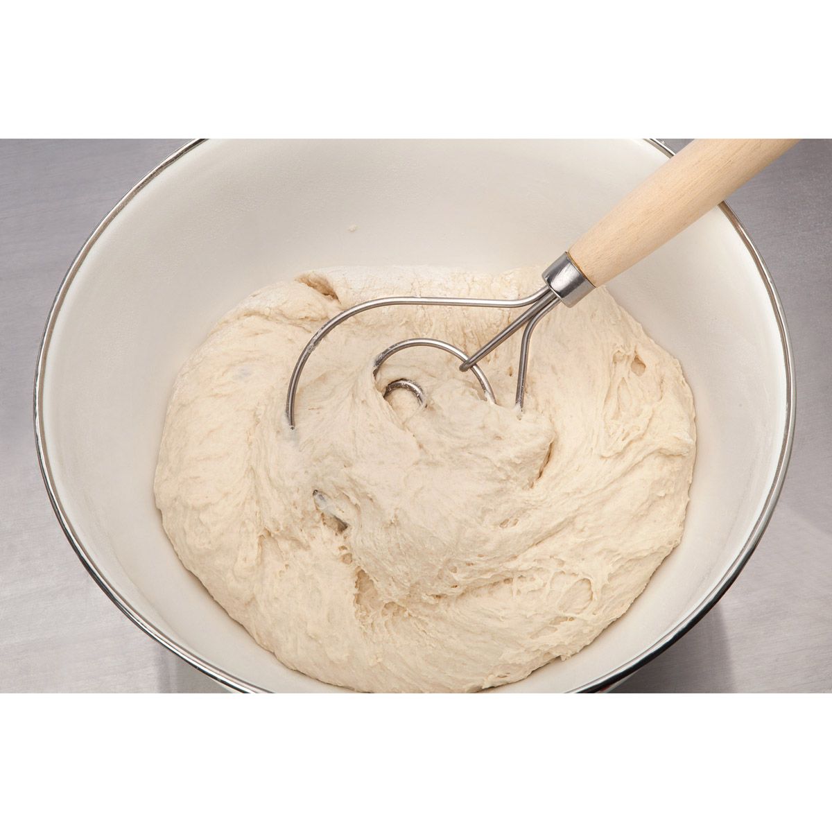 dough whisk displayed in a white bowl filled with dough on a gray surface