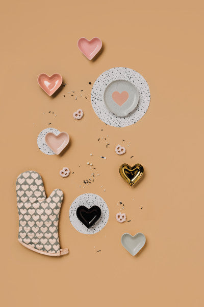 multiple different color heart pinch bowls displayed next to a heart oven mitt heart plates and pretzels on a pale orange background