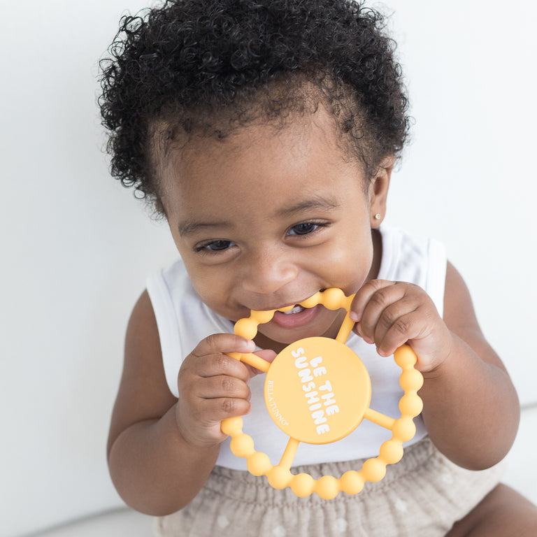 baby girl chewing on happy teether against a white background