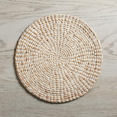 round woven hyacinth placemat with white-wash finish on a grey wooden background.