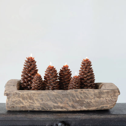 lit pine cone shaped candles in a wooden bowl.