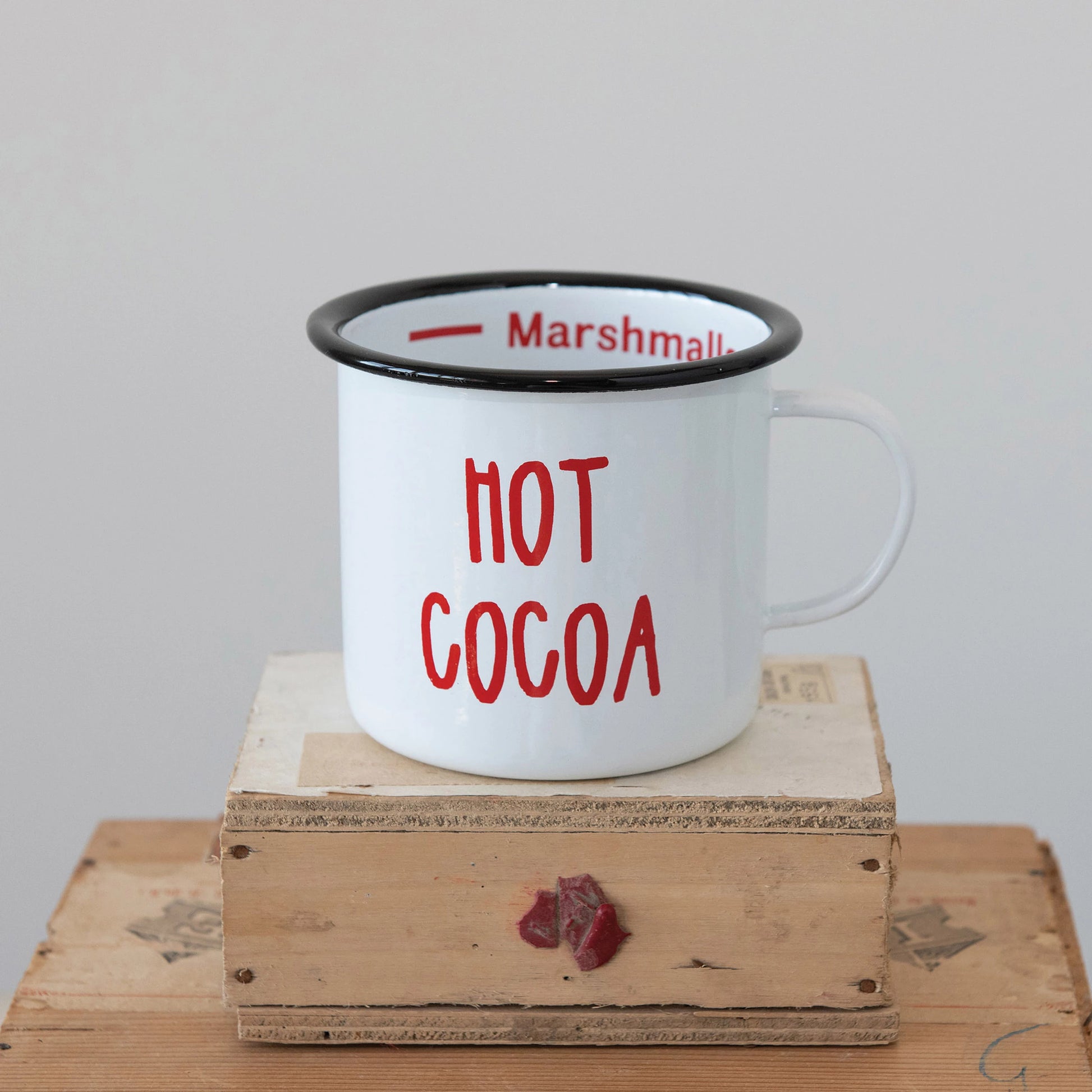 white tin mug with a black rim and hot cocoa written in red.