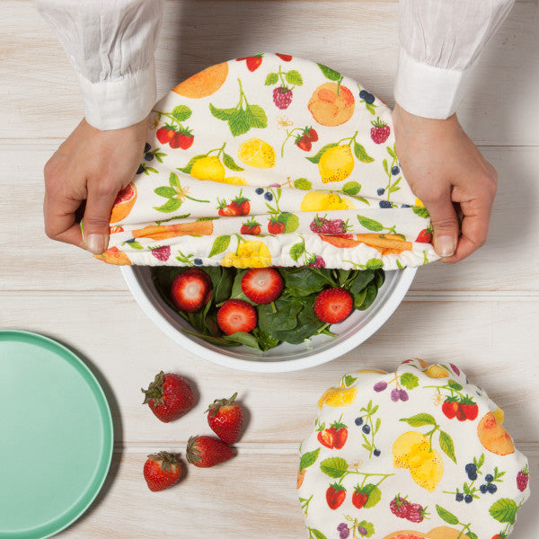 hands putting fruit salad bowl cover onto a bowl filled with salad.