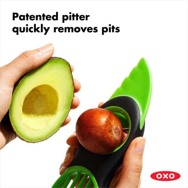 hand holding half an avocado and slicer with pit on it.