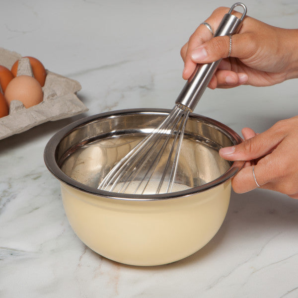 hands holding bowl and whisk stirring ingredients in bowl.