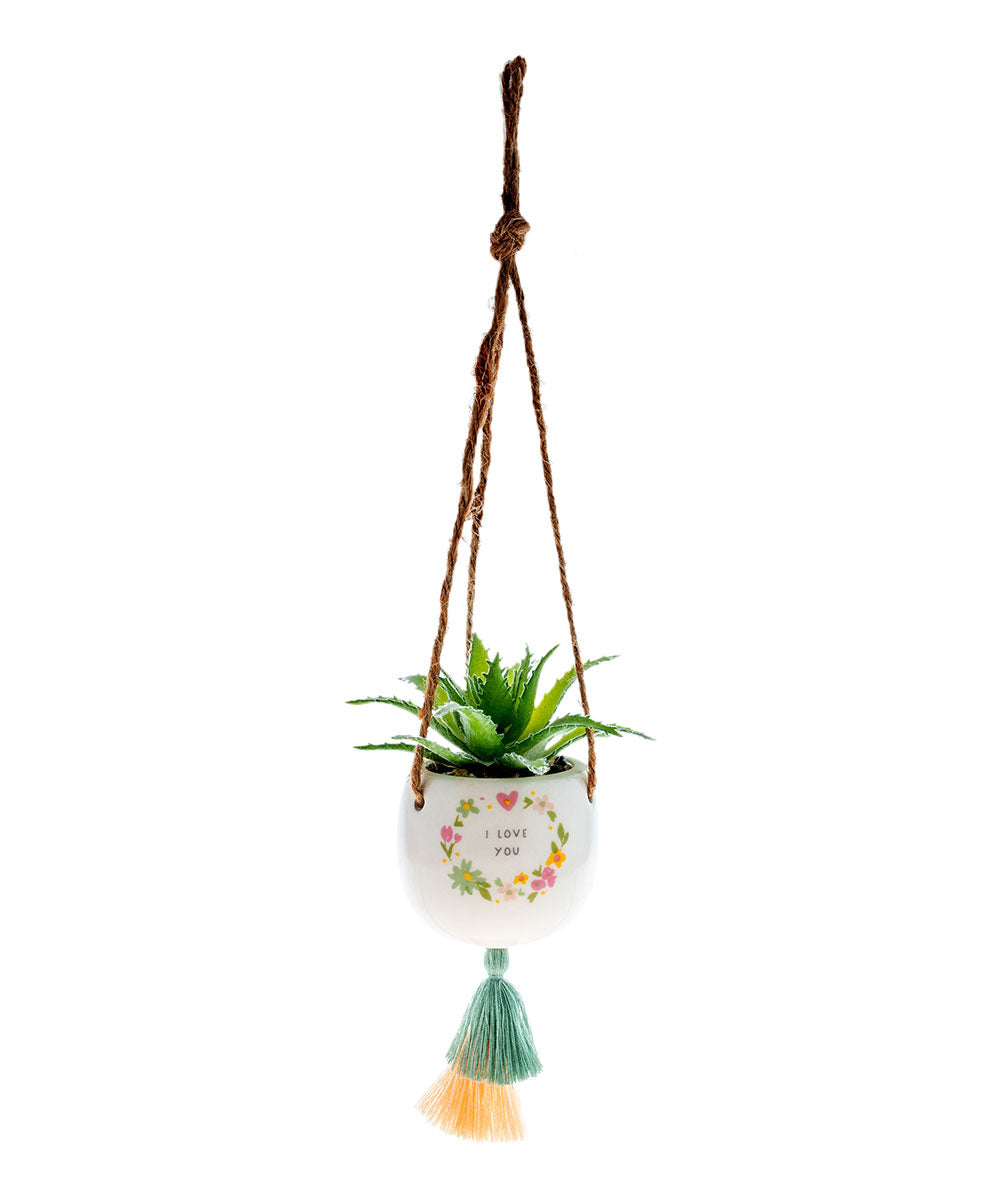 small ceramic pot with a succulent in it hanging form jute twine with a tassel on the bottom, a floral wreath with " i love you" printed on it.