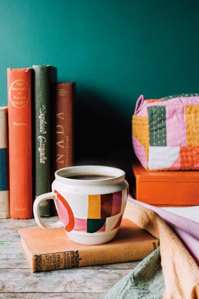 prism formation mug displayed on a table with books, matching zipper bag, and napkin against a teal wall