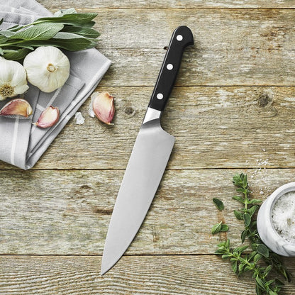 chef's knife on wooden board surrounded by herbs and a towel.